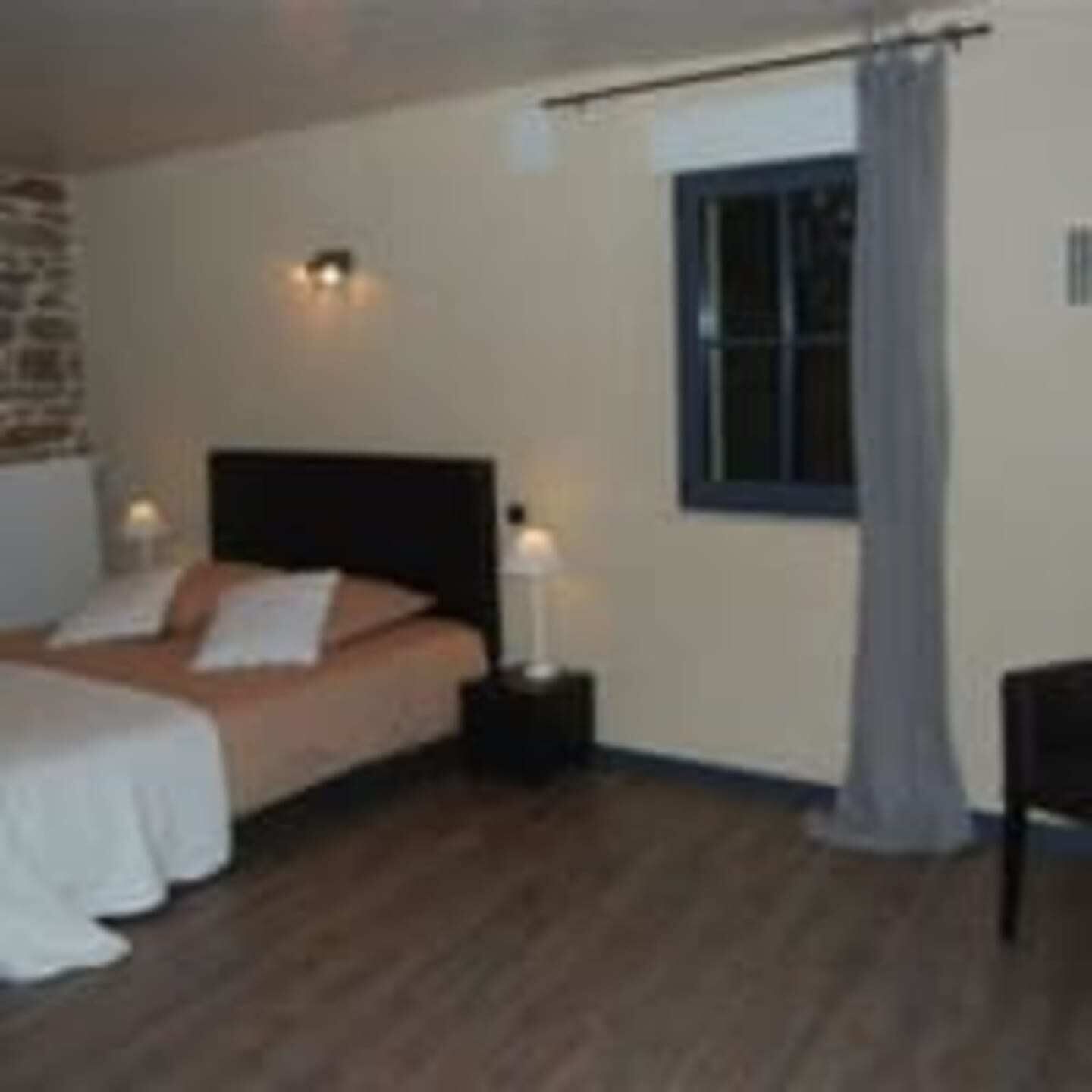 Une chambre à coucher comprenant un lit, des tables de chevet, une fenêtre avec un rideau et un luminaire fixé au mur.