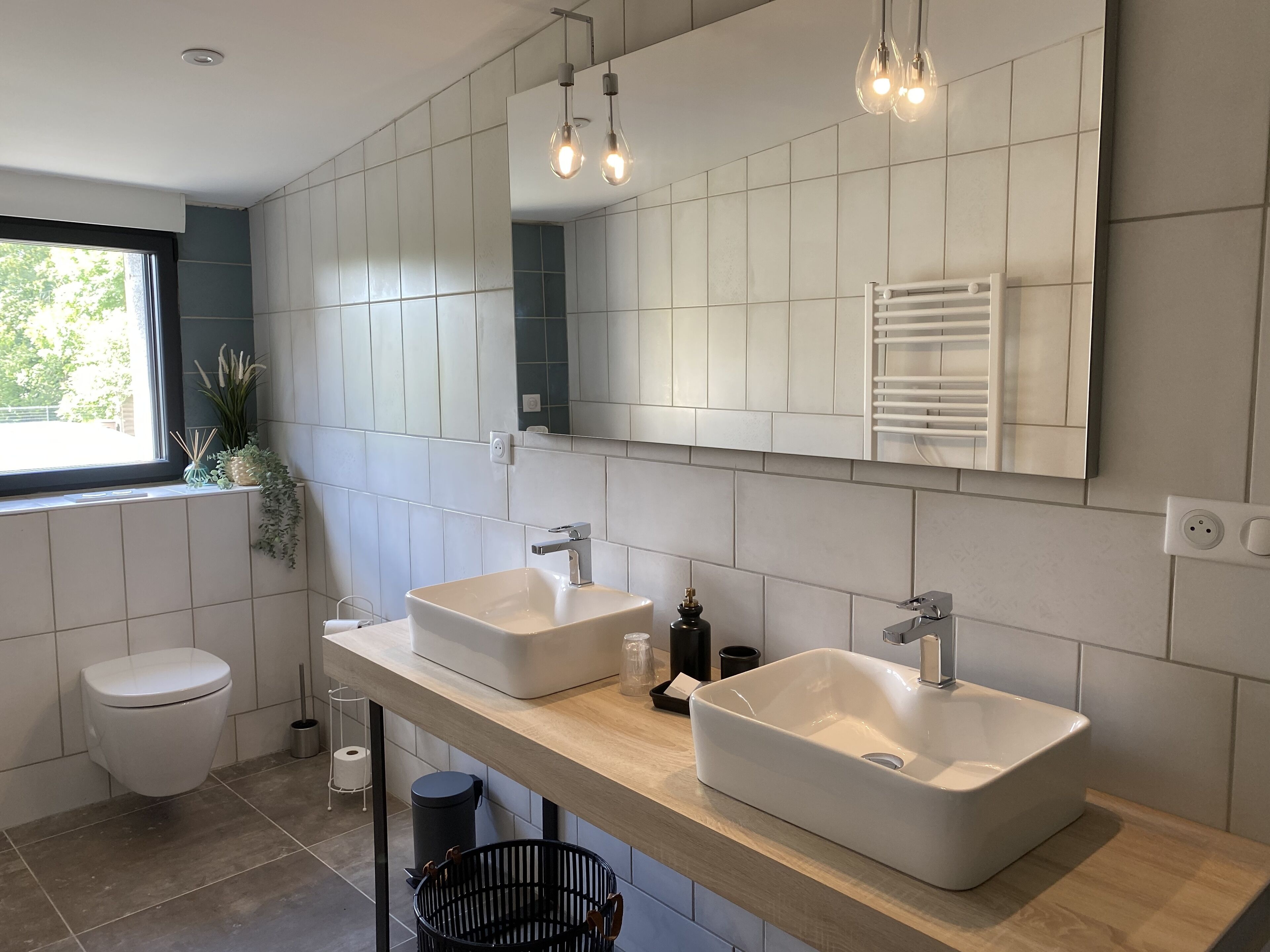 Un baño moderno con dos lavamanos, un inodoro, una ventana y un espejo.
