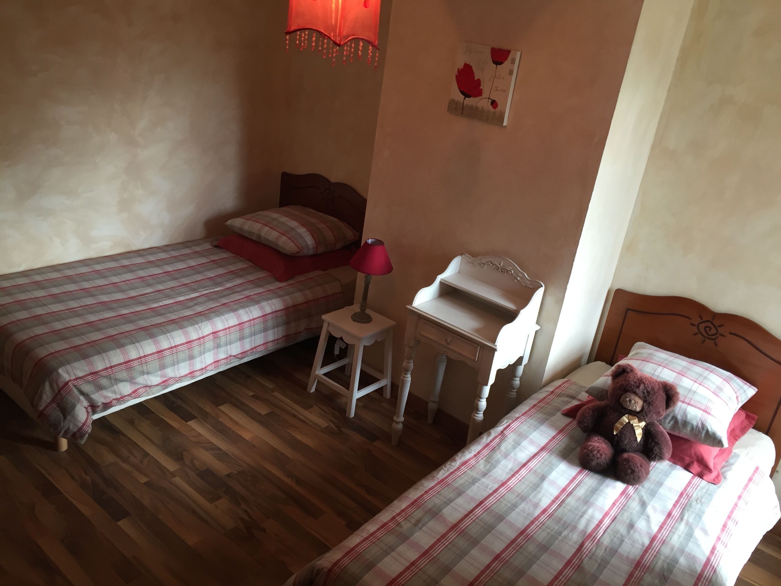 Ein Schlafzimmer mit zwei Betten, einem Nachttisch, einem kleinen Tisch und einem Teddybär auf einem Bett.