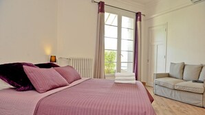 A bedroom with a large bed, a bedside table with a lamp, a window with curtains, a radiator, and a sofa. - Air-conditioned apartment 100m2 garage terrace near Avignon center (Avignon)