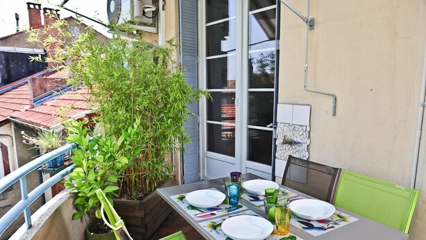A small balcony with a table set for two, surrounded by potted plants and a view of neighboring buildings. - Air-conditioned apartment 100m2 garage terrace near Avignon center (Avignon)