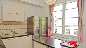 A modern kitchen with white cabinets, a stainless steel refrigerator, a black countertop, and a window with striped curtains. - Air-conditioned apartment 100m2 garage terrace near Avignon center (Avignon)