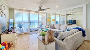 Un salon spacieux avec un grand canapé, une table basse et un téléviseur. Il y a un balcon avec vue sur l’océan.