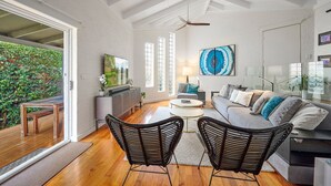 A spacious living room with a large window, a ceiling fan, a sofa, two armchairs, a coffee table, and a TV.