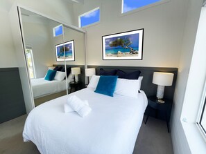 A hotel room with a large bed, two bedside tables, a mirror, and a framed picture of a beach scene.