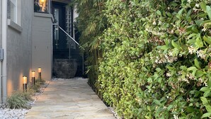 A stone pathway leading to a building with a large window and a staircase.