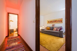 A hallway with a patterned rug leading to a living area with a sofa and a colorful painting on the wall.
