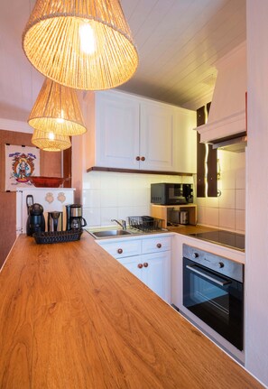 A kitchen with white cabinets, a wooden countertop, a microwave, a coffee maker, and a hanging light fixture.