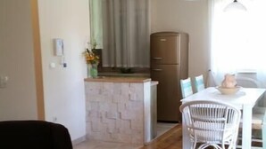 A living room with a sofa, a dining table with chairs, a kitchen area with a refrigerator, and a window with curtains. - Apartments Villa Rustica (ST) - Two-Bedroom Apartment with Balcony and Shared Pool (groundfloor) (Zadar)