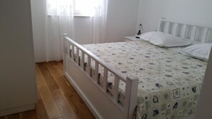 A bedroom with a wooden floor, a bed with a floral bedspread, a white headboard, and a nightstand with a lamp. - Apartments Villa Rustica (ST) - Two-Bedroom Apartment with Balcony and Shared Pool (groundfloor) (Zadar)