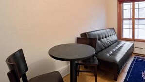 A living room with a dark leather sofa, a round table, and two chairs. - Pizo Lodge (Kabwe)