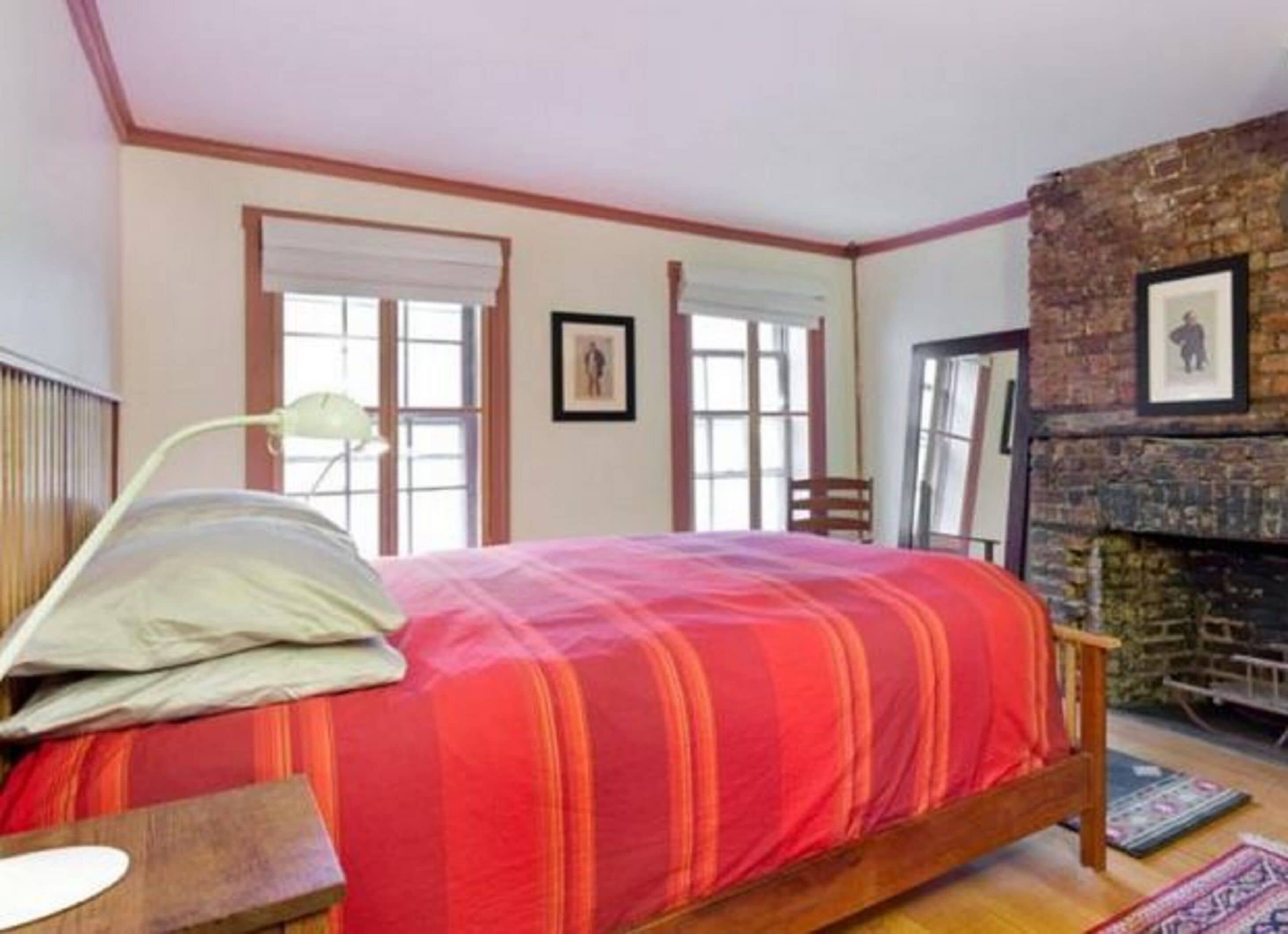 A bedroom with a bed, a lamp, a chair, a fireplace, and a window.