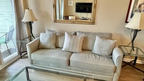 Ein Wohnzimmer mit einem beigefarbenen Sofa, zwei Nachttischen mit Lampen, einem Glastisch und einem großen Spiegel an der Wand.