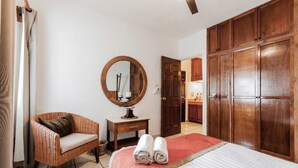 A bedroom with a bed, a chair, a dresser, a mirror, and a door leading to a bathroom.