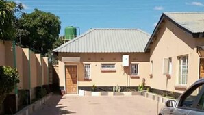 A paved driveway leading to a building with a metal roof and a car parked on the right. - Mwayose Lodge (Lusaka)