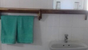 A bathroom with a sink, a mirror, a towel rack with a green towel, and a trash can. - Mwayose Lodge (Lusaka)