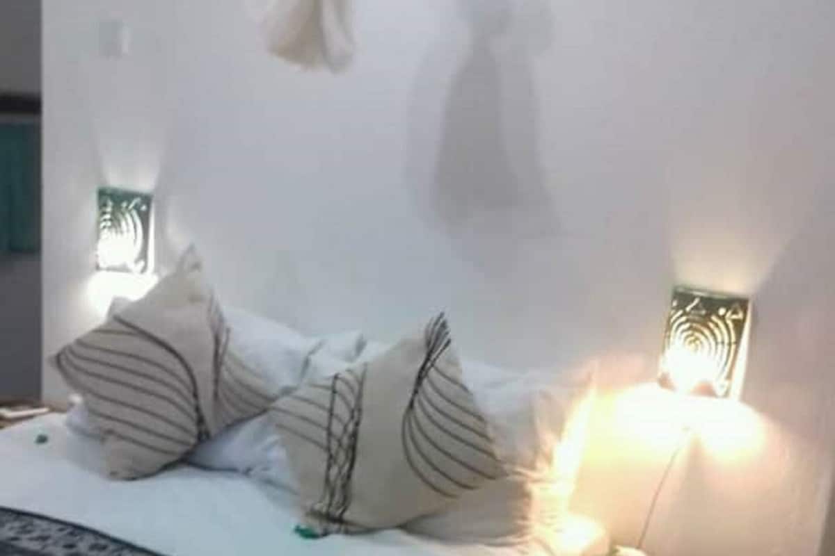 Cama bem arrumada com roupa de cama estampada, mesa de cabeceira com caixa de lenços e duas luminárias fixadas na parede.