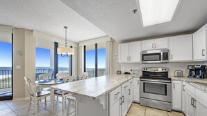 Une cuisine moderne avec des meubles blancs, un grand îlot central et une vue sur l’extérieur.