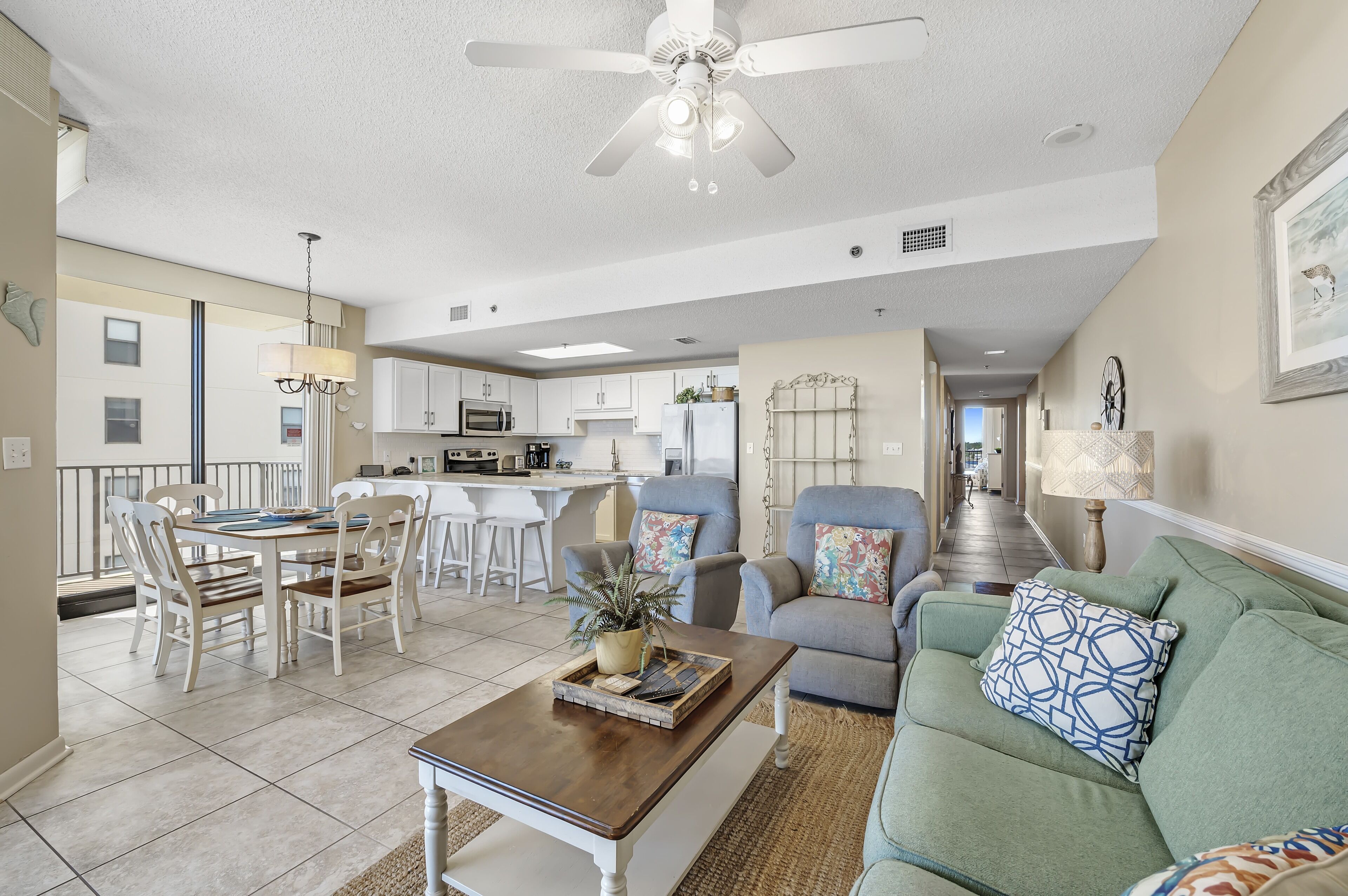 A spacious living room with a dining area, a kitchen in the background, and a balcony with a railing.