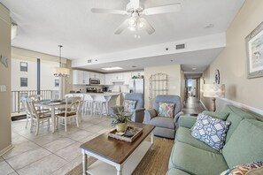 A spacious living area with a dining table, sofas, and a ceiling fan.