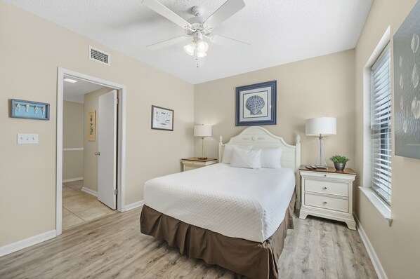 A bedroom with a bed, nightstands, a ceiling fan, and a window with blinds.