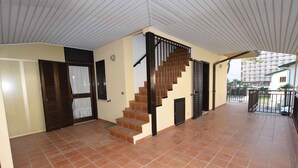 Un espacio interior amplio con suelo de baldosas, una escalera de madera con barandales negros y una puerta con ventanal.