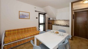 Una habitación pequeña y acogedora con sofá, mesa de comedor con sillas, zona de cocina y una puerta.