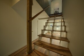 Una escalera de madera con un rascador para gatos a la izquierda, que conduce a un rellano con una puerta y una ventana.