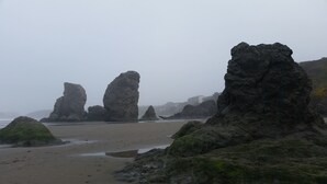 Une plage avec de grandes formations rocheuses et une rive sablonneuse.