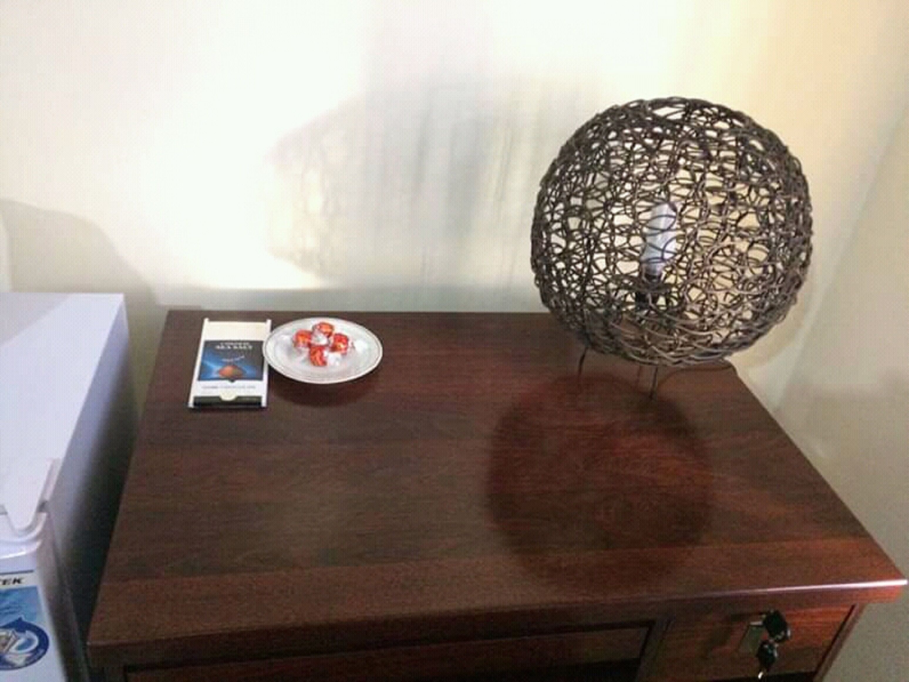 Une table de chevet en bois ornée d’une sphère métallique décorative, une assiette contenant des objets rouges et un livre.