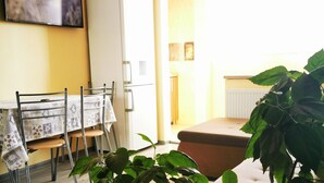 A dining area with a table and chairs, a white refrigerator, and a television on the wall. - Ultra Central apartment (Oradea)