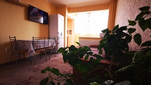A living room with a dining table, chairs, a TV, a refrigerator, and a large window with curtains. - Ultra Central apartment (Oradea)