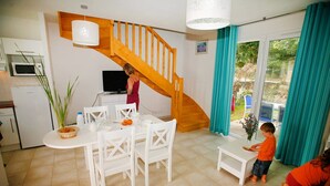 Une cuisine moderne avec des appareils électroménagers blancs, un coin repas avec des chaises blanches et un escalier en bois.