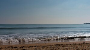 Une plage où les vagues se brisent près du rivage, un ciel dégagé et une terre lointaine à l’horizon.