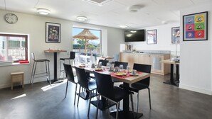 A modern dining area with a long table, black chairs, and a window with a view.