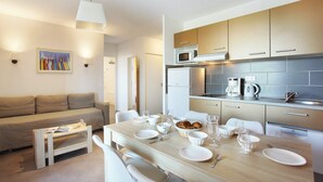 A modern kitchen with a dining area, featuring a wooden table set for four, a sofa, and a coffee machine.