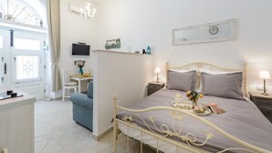 A bedroom with a bed, bedside tables, a desk, a chair, a television, and a window with curtains.