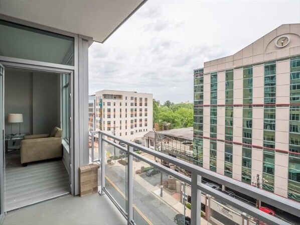 A balcony with a sofa and a lamp, overlooking a cityscape with modern buildings and a clear sky.