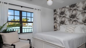 Ein Schlafzimmer mit einem Bett, einem Sessel, einem Fenster mit Vorhängen und einem Deckenventilator.