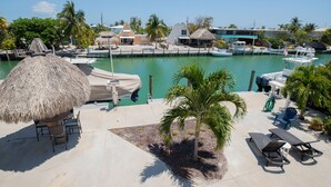 Ein Yachthafen mit vertäuten Booten, einem Reetdach-Sonnenschirm, Liegestühlen und einem Poolbereich mit Palmen.