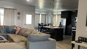 A modern living room with a sectional sofa, a dining area with a kitchen in the background, and a ceiling fan. - Sand Hollow Retreat (Hurricane)