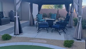 A covered patio area with outdoor furniture, including chairs and a table, under a pergola with curtains. - Sand Hollow Retreat (Hurricane)