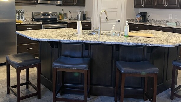 A modern kitchen with dark wood cabinets, a granite countertop, and a central island with bar stools. - Sand Hollow Retreat (Hurricane)