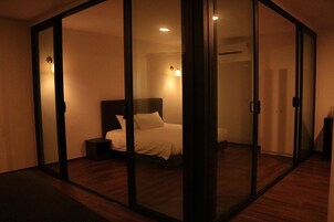 A bedroom with a bed, a nightstand, and a sliding glass door leading to another room.