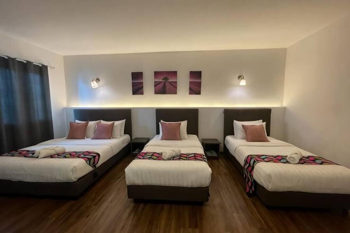 A hotel room with three beds, a wooden floor, and wall-mounted artwork.