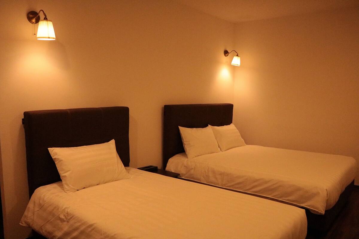 Two single beds with headboards, a wall-mounted light fixture, and a plain wall.