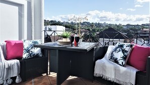 Un balcón con mobiliario de mimbre, una mesa y vista panorámica de la ciudad.