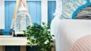 Un dormitorio con cama blanca, paredes azules y una mesita de noche con lámpara y planta.