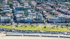 Vista aérea de una zona urbana costera con edificios residenciales, una playa y un paseo marítimo.