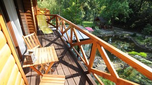 Une terrasse en bois, agrémentée de chaises et d’une table, qui offre une vue sur un étang et la verdure environnante.